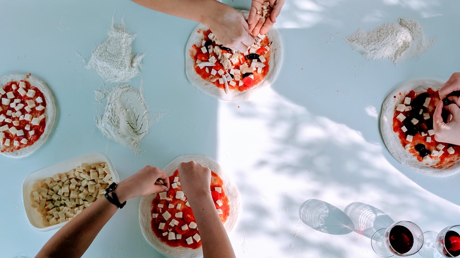 Top-down photograph of people putting toppings on pizza