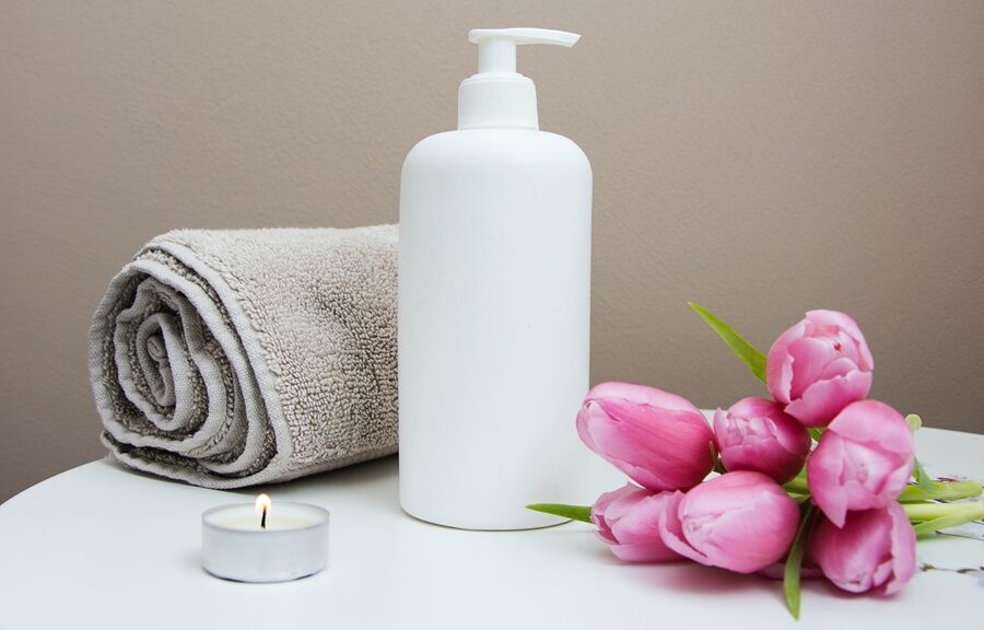 Image of a towel, some tulips, a tea light, and a soap dispenser on a white table