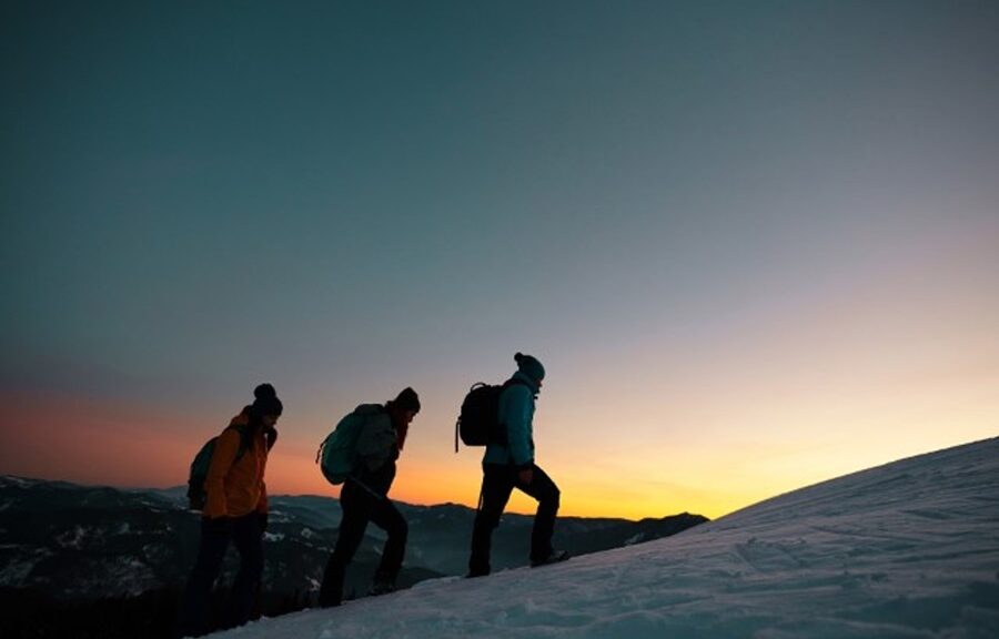 Three people walking on a snow covered hill at dusk